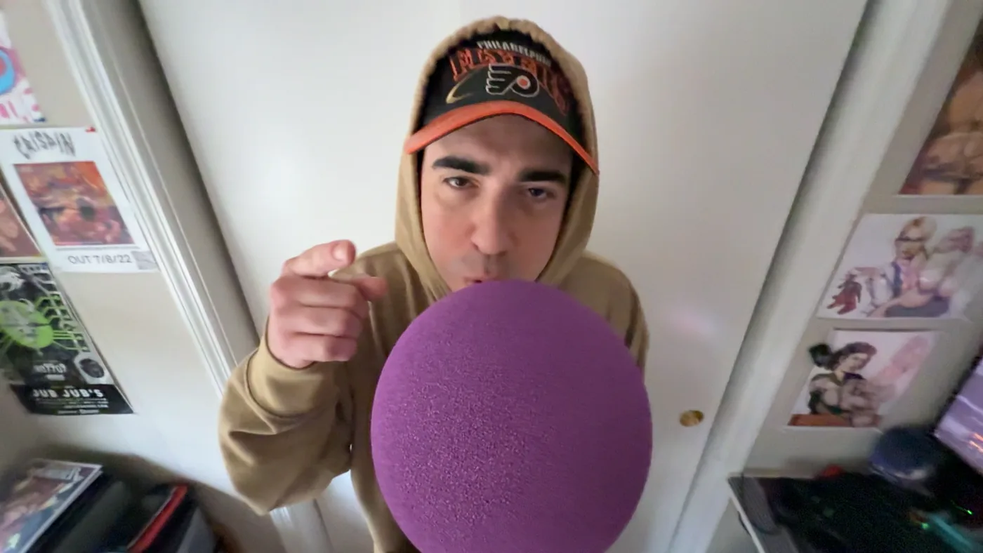 Horus rapping into a purple mic cover in a cluttered room